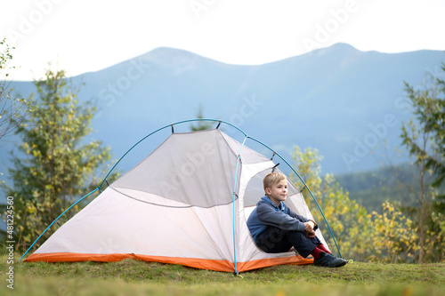 Hiker child boy resting in a tourist tent at mountain campsite enjoying view of beautiful summer nature.