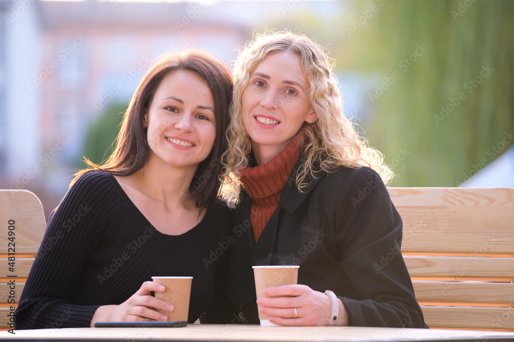 Portrait of two happy young women sitting at city street cafe