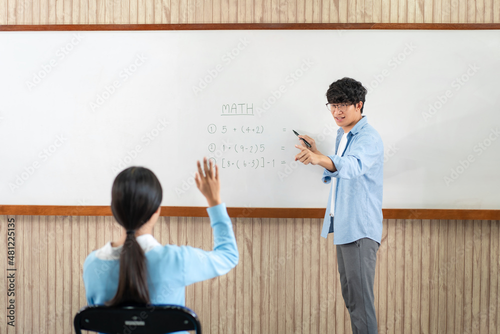 Male tutor standing in front of whiteboard is smiling and pointing to him for ask question and asian young boy Male tutor standing in front of whiteboard is smiling and pointing to him for ask question and asian young boy