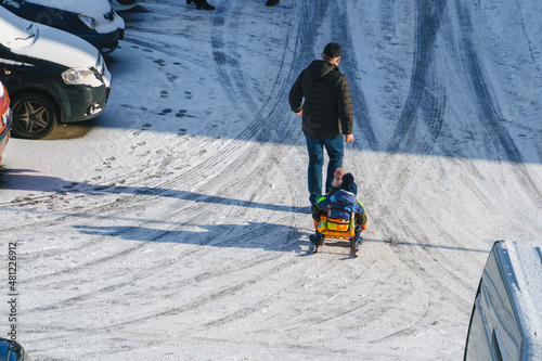 Father sledding children on a snowy road on a sunny winter day, joint winter games of children and adults