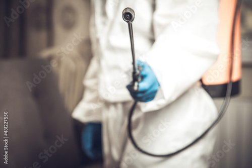 Spray gun with pesticides close-up. An exterminator in work clothes sprays pesticides from a spray bottle. Fight against insects in apartments and houses. Disinsection of premises