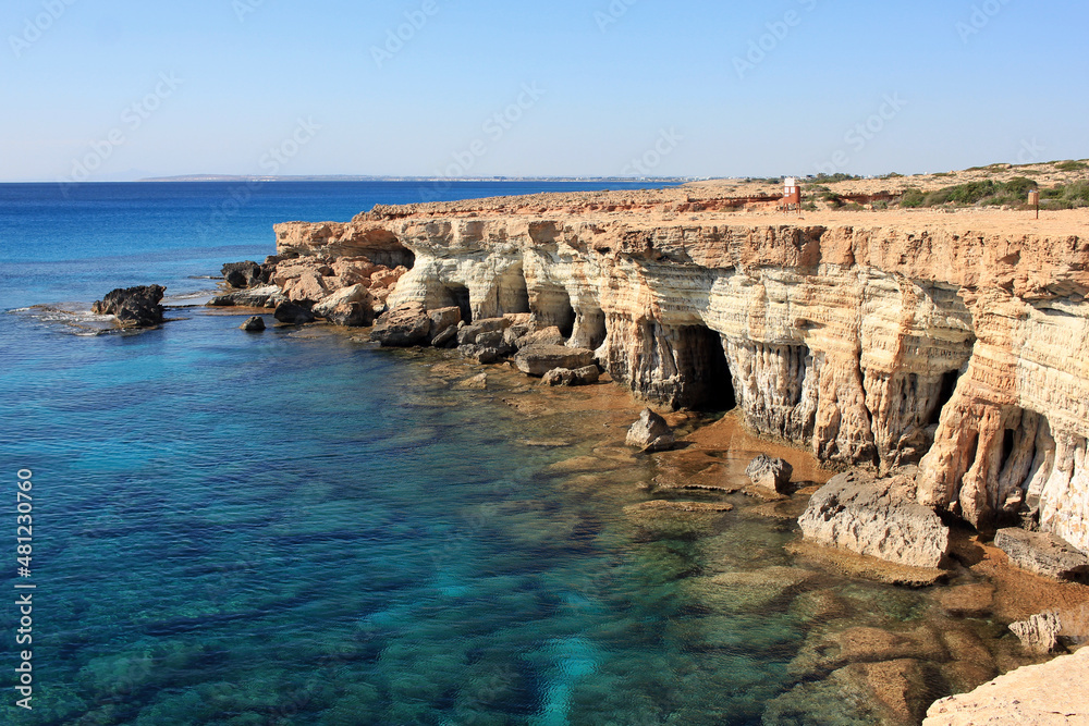 A view of a small lagoon with clear cyan water and a sea shore with sea caves in Kavo Greko, near touristic city Aiya Napa, Cyprus