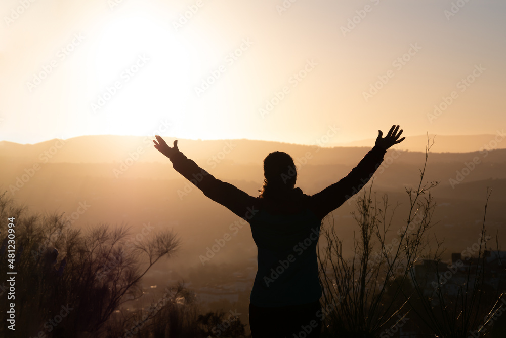 Silhouette of woman raising arms mountain at dawn