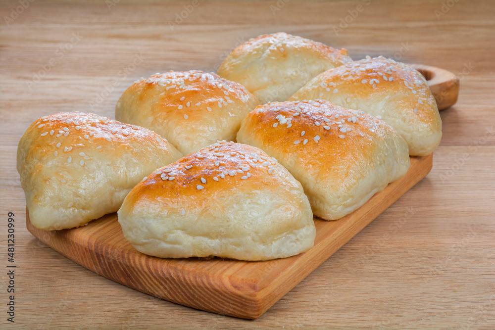 Fresh baked fragrant buns sprinkled with sesame stacked on a wooden kitchen board