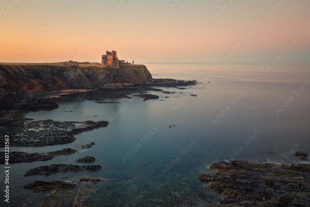 The ruins of an old castle standing on a cliff on the shore of the sea bay at sunset. Scotland 