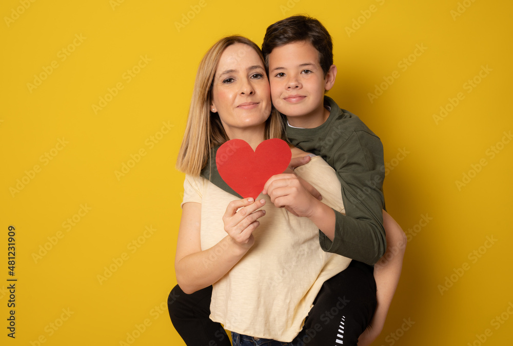 Happy mother and son together holding heart isolated over yellow background. Happy mother and son together holding heart isolated over yellow background.