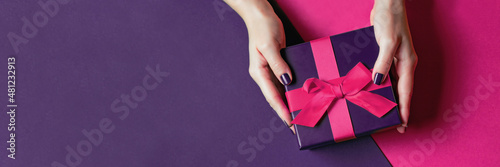 Women's hands with beautiful manicure hold a gift. Banner with a pink bow on a purple background. Gift box for the holiday