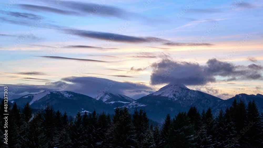 Clouds forming over the mountains at dusk. Trees in the foreground covered with snow. Colorful sky Clouds forming over the mountains at dusk. Trees in the foreground covered with snow. Colorful sky