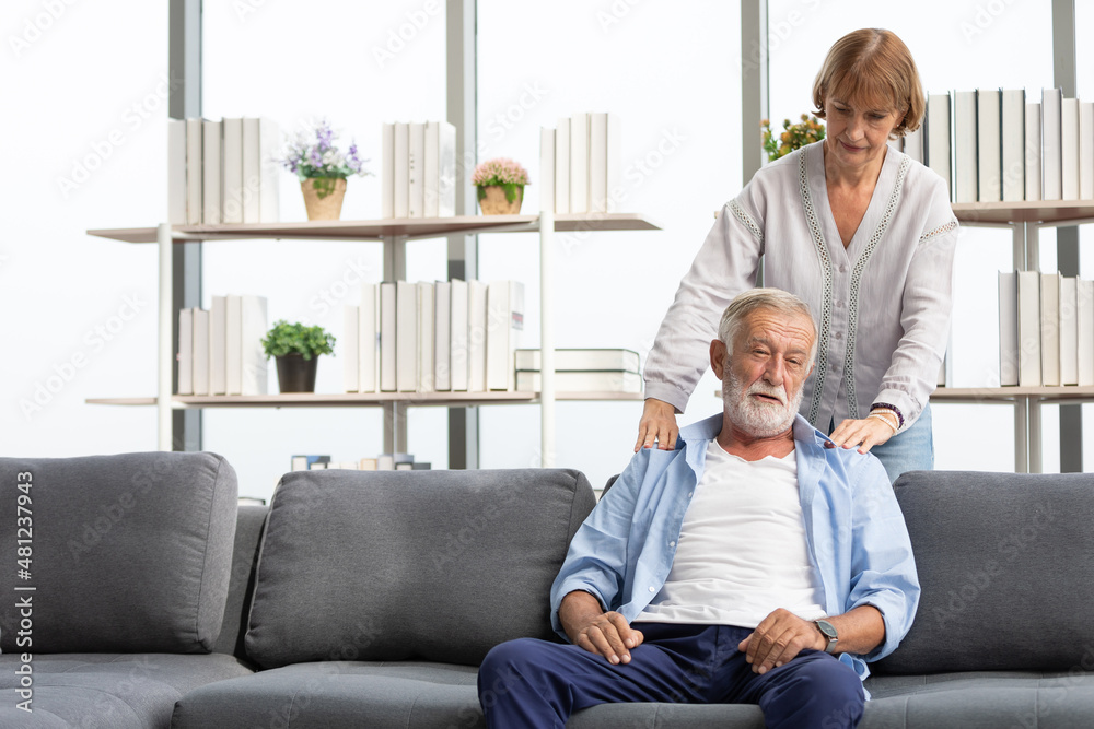 senior woman giving a shoulder massage to her husband on sofa senior woman giving a shoulder massage to her husband on sofa