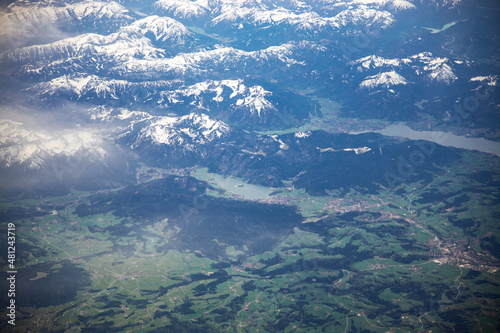 White clouds taken from a moving airplane. Green nature and mountains with snow below. Flying in air. Plane ride travel. High quality photo