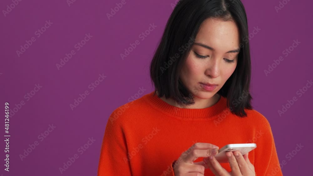 Confident woman in red sweater typing on phone in the purple studio Confident woman in red sweater typing on phone in the purple studio