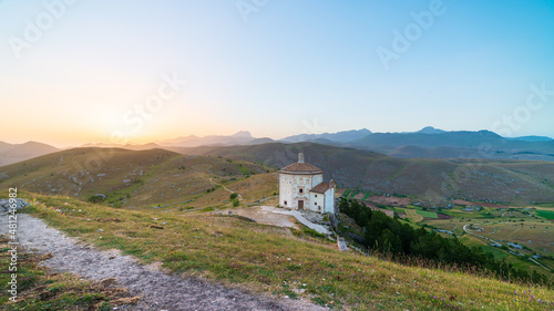 The small octagonal chapel near Rocca Calascio castle ruins at sunset in backlight, landmark in the Gran Sasso National Park, Abruzzo, Italy. Mountains scenic background.