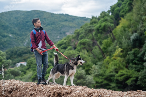Handsome hiker boy with Siberian husky dog looking at beautiful view in mountains © iwavephoto