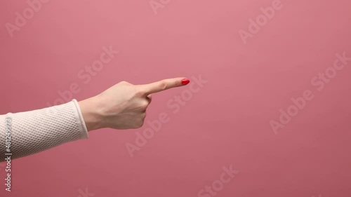 Profile side view closeup of woman hand pointing to someting with index finger, showing copyspace for advertising area. Indoor studio shot isolated on pink background. photo