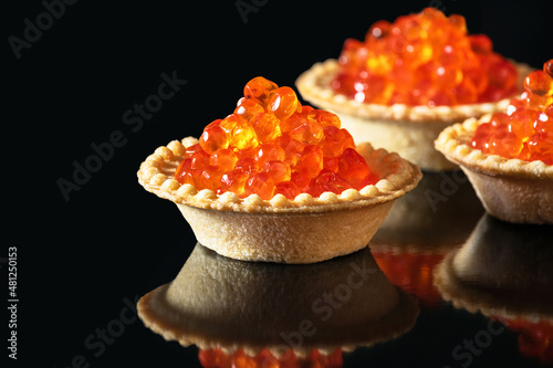 Red caviar in tartlets over black background. Close-up salmon caviar. Delicatessen. Gourmet food. Texture of caviar. Seafood