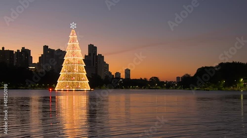 Beautiful city lake at dusk with christmas tree floating, some buildings around and the water of the lake reflecting the buildings.Video at Igapo Lake, Londrina city, Parana state, Brazil. Zoom out. photo
