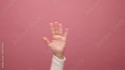 Closeup of woman hand waving hand, showing palm, making hello or good bey gesture, greeting or acclaiming. Indoor studio shot isolated on pink background. photo