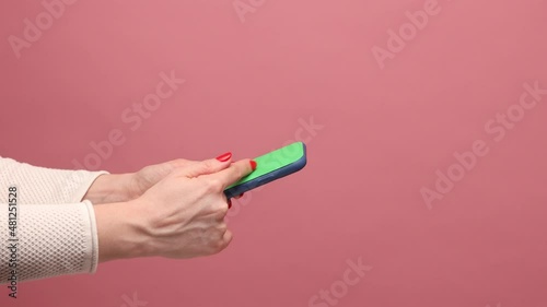 Profile side view closeup of woman hand holding mobile phone in hand, crolling online, surfing internet website. Indoor studio shot isolated on pink background. photo