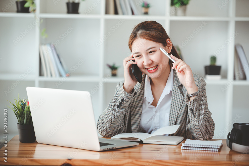 Businesswoman or accountant using the phone to check business information. Accounting Documents and Laptop at Small Office Business Ideas Businesswoman or accountant using the phone to check business information. Accounting Documents and Laptop at Small Office Business Ideas