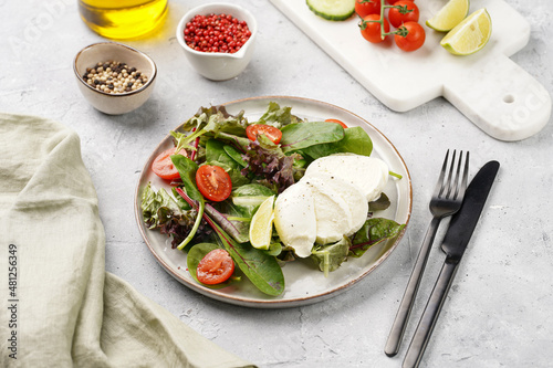 Salad with green leaves, lettuce, spinach, cherry tomatoes, mozzarella, olive oil, chilli pepper, lime juice on grey stone surface