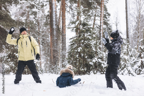 Father and sons having fun snowball fight together in winter forest. Happy children playing in snow outdoors. Christmas holidays, New year family vacation. Brothers in warm clothes walking in cold day