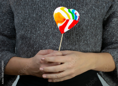 Colorful heart-shaped lollipop in the hands of a young girl. photo