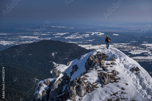 Man stands on summit of Teufelstaettkopf on ski tour in winter and looks over the snowy valley of the Ammergau Alps in Bavaria in winter. © Bastian Linder