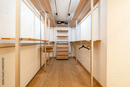 Trendy white dressing room with luminous lamps and a parquet on the floor. There are lockers, shelves and hangers for clothes and shoes