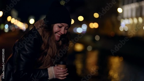 cheerful woman with cup of coffee to go in city embankment in night