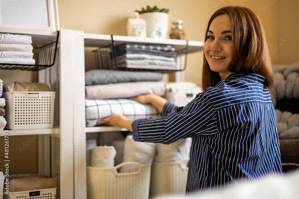 Domestic woman in pajamas neatly putting folded linens into cupboard vertical storage Marie Kondo Domestic woman in pajamas neatly putting folded linens into cupboard vertical storage Marie Kondo