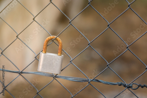 A rusted and forgotten padlock on a wire fence
