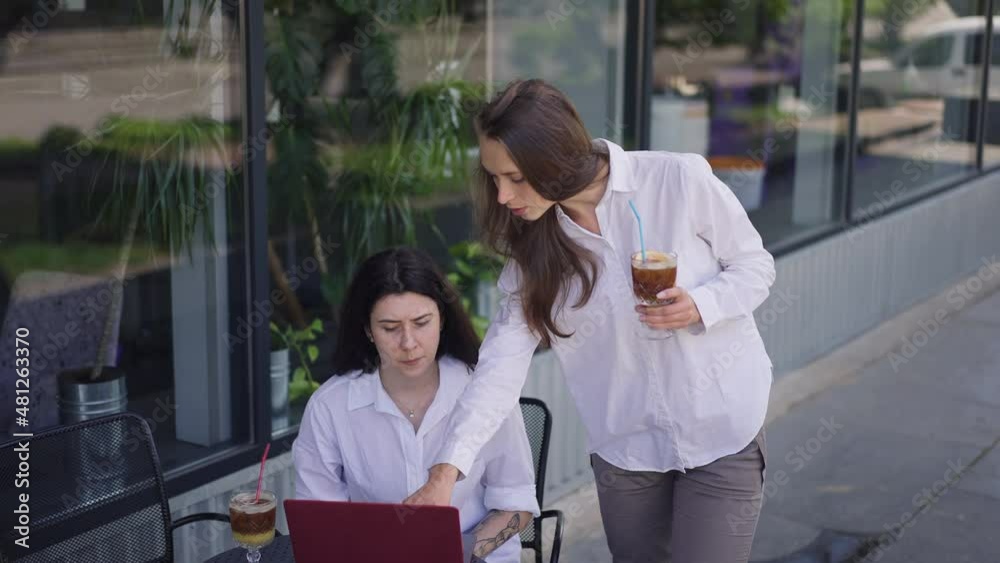 Two confident young women discussing startup project on cafe summer terrace with drinks. Concentrated Caucasian coworkers brainstorming on lunch break outdoors talking planning strategy idea Two confident young women discussing startup project on cafe summer terrace with drinks. Concentrated Caucasian coworkers brainstorming on lunch break outdoors talking planning strategy idea