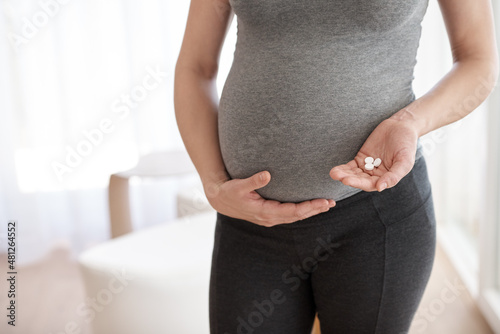 Prenatal vitamins. Cropped shot of a pregnant woman holding tablets while standing in her home.