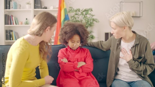 Unhappy little black girl sitting on couch lgbt parents scolding kid for mistake photo