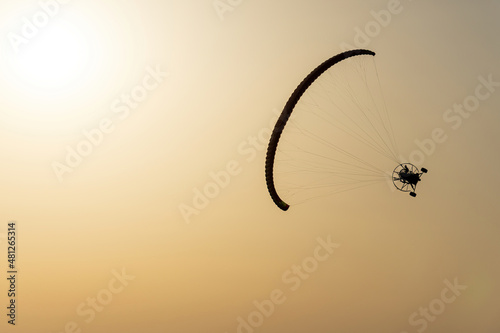 Paramotor vehicle tilted flying in a yellow sky by the sun