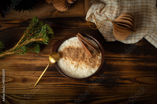 Scandinavian-style rice porridge. The rice pudding is in a blue ceramic bowl on a wooden table, with gingerbread cookies, cinnamon and dried orange slices.