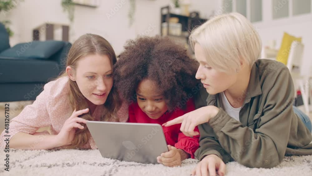 Happy gay parents and little black daughter using tablet on floor family leisure Happy gay parents and little black daughter using tablet on floor family leisure