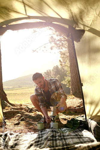 Into the woods. Shot of a young man making coffee on a camp stove while camping.