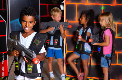 Emotional afro-american boy with laser pistol playing laser tag with friends on dark labyrinth. High quality photo