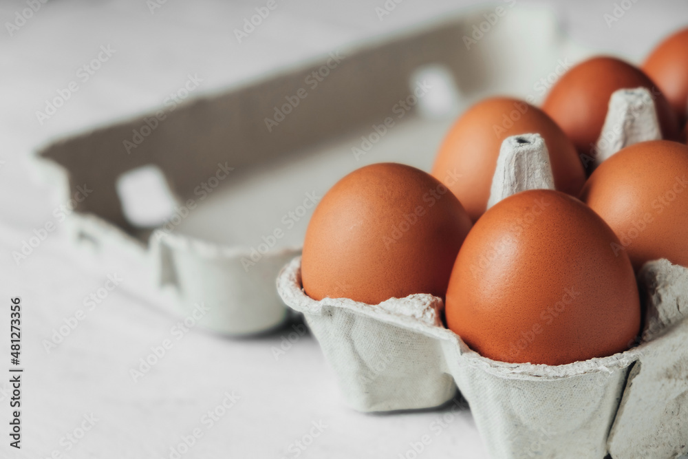 Brown chicken eggs in cardboard tray on white wooden table. Side view of an open container with eggs. Brown chicken eggs in cardboard tray on white wooden table. Side view of an open container with eggs.