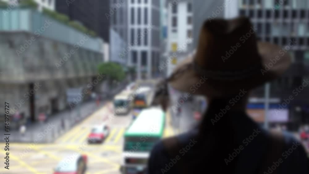 Blurred defocused tourist asian woman wear a hat in pedestrian bridge looking traffic on road with red taxi cars and buses at street of Hong Kong. Busy lifestyle in central city Blurred defocused tourist asian woman wear a hat in pedestrian bridge looking traffic on road with red taxi cars and buses at street of Hong Kong. Busy lifestyle in central city