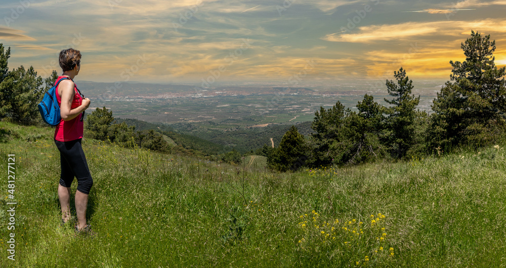 Obraz premium Girl with blue backpack and sport clothes, enjoying from the mountain valley in magical moments.