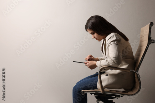 Young woman with bad posture using tablet while sitting on chair against grey background. Space for text