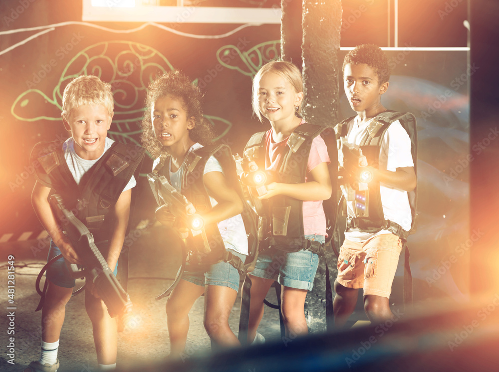 Cheerful tween girls and boys of different nationalities with the laser pistols posing together in a dark laser tag labyrinth