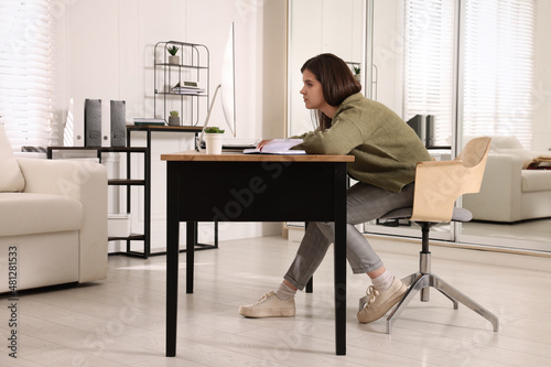 Young woman with bad posture working at table in office