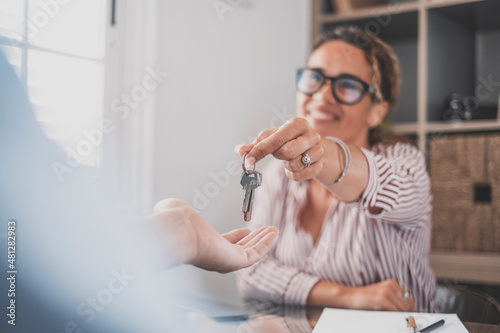 Smiling female realtor agent giving keys to apartment buyer. Homeowner receiving their new house key from a real estate agent at office. Happy saleswoman giving house keys to customer photo