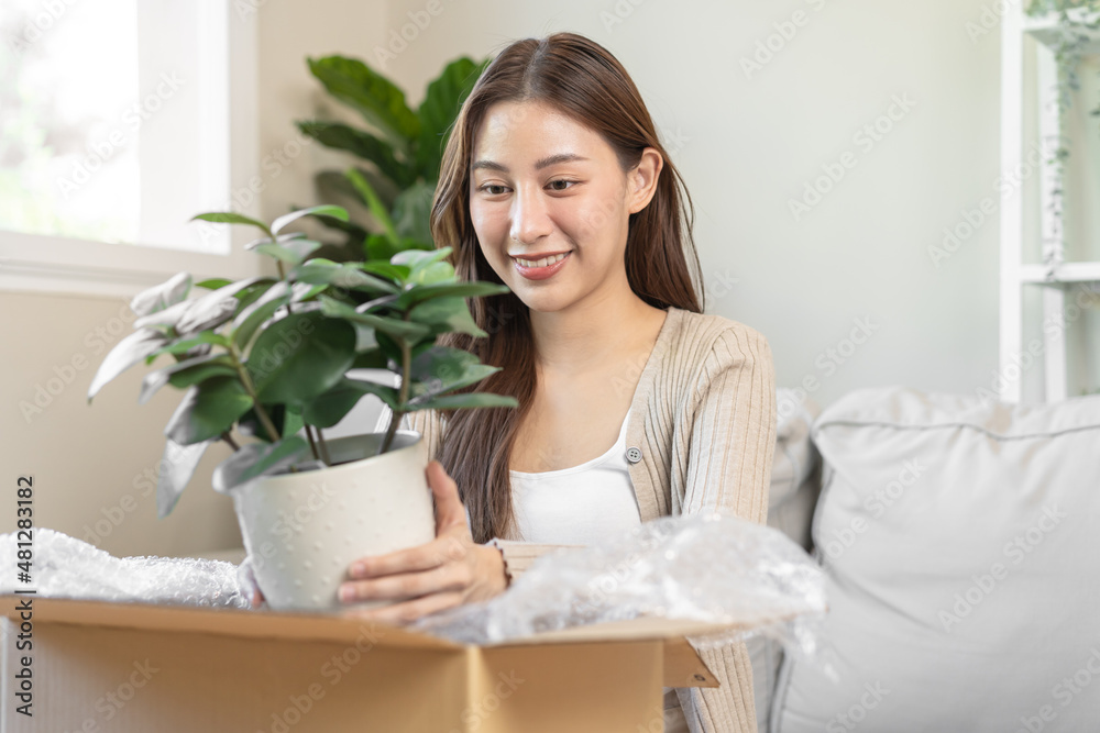Happy asian young woman, customer received, unpack package carton open parcel in cardboard box, holding ceramic plant pot. Moving, preparing in new house, relocation. Online shop delivery at home. Happy asian young woman, customer received, unpack package carton open parcel in cardboard box, holding ceramic plant pot. Moving, preparing in new house, relocation. Online shop delivery at home.
