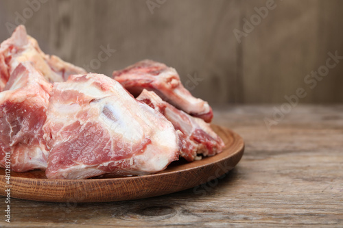 Plate with raw chopped meaty bones on wooden table, closeup. Space for text