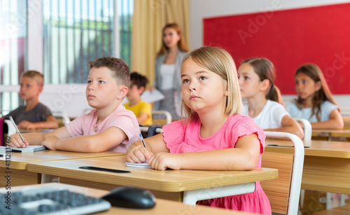 Portrait of tired schoolgirl sitting in classroom during lesson in elementary school