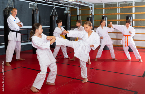 Group of preteen children practicing taekwondo kicks in pairs at sport gym